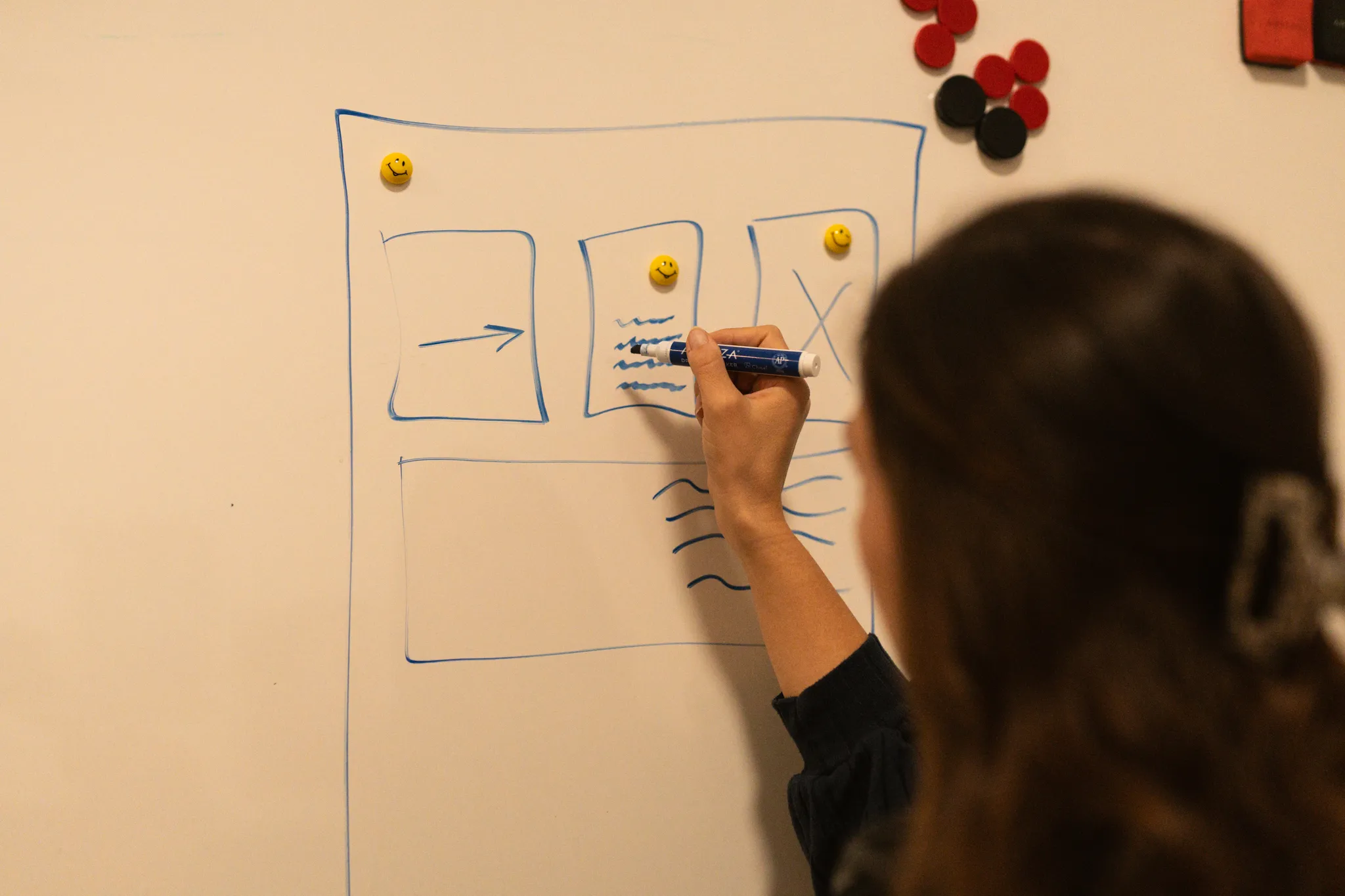 Person zeichnet auf einem Whiteboard, mit Smartphone und Dokumenten auf dem Tisch