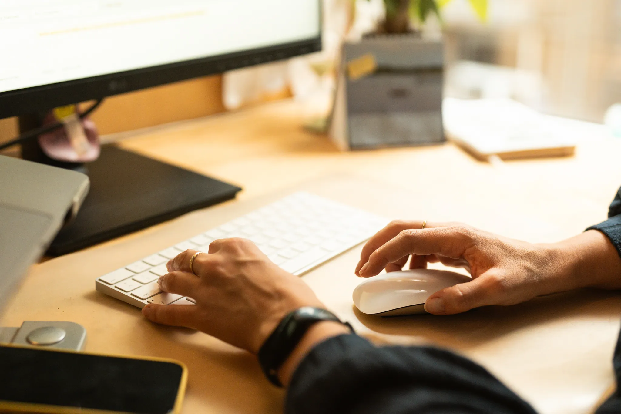 Hände einer Person tippen auf einer Tastatur und benutzen die Maus auf dem Schreibtisch